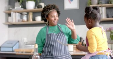 Mutlu Afrika kökenli Amerikalı anne ve kız krep kızartıyorlar ve mutfakta beşlik çakıyorlar, ağır çekimde. Yaşam tarzı, aile, birliktelik, yemek, aşçılık ve ev hayatı, değişmemiş..