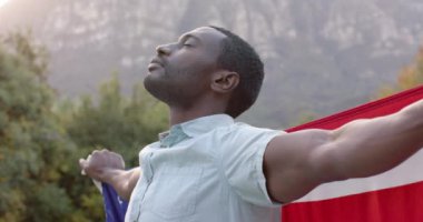 Bahçede Amerikan bayrağı taşıyan Afro-Amerikan bir adamın portresi, ağır çekimde. Vatanseverlik, kutlama ve yaşam tarzı değişmedi..