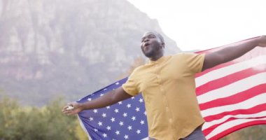 Portrait of african american man holding flag of usa in garden, slow motion. Patriotism, celebartion and lifestyle, unaltered.
