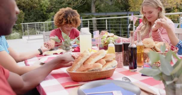 手を握り 庭のディナーテーブルで祈りを捧げる友人の多様なグループ ゆっくりとした動き 食べ物 トータルネスティ ライフスタイル 家庭生活 変わらない — ストック動画