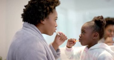 Afro-Amerikan anne ve kızının banyoda dişlerini fırçalaması, ağır çekim. Yaşam tarzı, kişisel bakım, hijyen ve ev hayatı, değişmemiş..