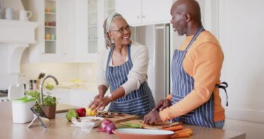 Önlüklü mutlu Afro-Amerikan çift mutfakta yemek hazırlıyor, ağır çekimde. Emeklilik, ev hayatı, yemek pişirme, birliktelik, sağlıklı yaşam ve kıdemli yaşam tarzı, değişmemiş.