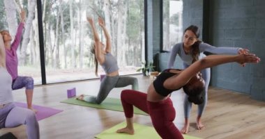 Farklı kadın eğitmenler, stüdyoda hilal pozu verirken kadınlara yardım ediyor. Değiştirilmemiş, yavaş çekim, yoga, egzersiz, fitness, zen, sağlıklı yaşam tarzı ve refah kavramı.