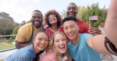 ABD bayrakları taşıyan ve bahçede selfie çeken mutlu arkadaş grupları, yavaş çekim. Arkadaşlık, birliktelik, iletişim, kutlama, vatanseverlik ve yaşam tarzı, değiştirilmemiş..