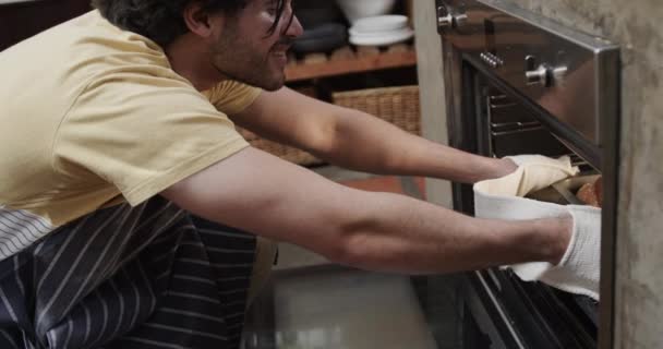 キッチンのオーブンからパンを取り出す幸せな白人男性 スローモーション 健康的なライフスタイル 食べ物 家庭生活 変わらない — ストック動画