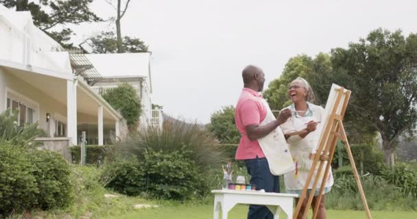庭の木製のイーゼルに幸せなシニアアフリカ系アメリカ人のカップル絵画 スローモーション 国内生活 創造性 団結とシニアライフスタイル 変更されません — ストック動画