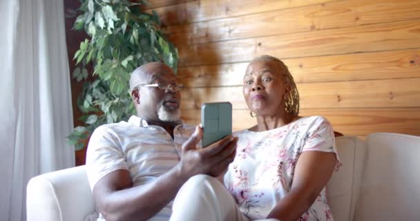 Ευτυχισμένο Ζευγάρι Αφροαμερικανών Ηλικιωμένων Που Χρησιμοποιούν Smartphone Καθισμένοι Στον Καναπέ — Αρχείο Βίντεο