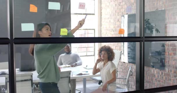 議論中の多様な男性と女性の同僚 オフィスのガラス壁でブレインストーミング ゆっくりとした動き ビジネス チームワーク ブレインストーミング ミーティング カジュアルオフィス — ストック動画