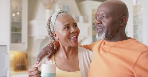 Lykkelig Afroamerikansk Senior Par Som Omfavner Drikker Kaffe Kjøkkenet Sakte – stockvideo