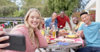 Mutlu bir grup arkadaş bahçede yemek masasında selfie çekiyorlar, ağır çekimde. Arkadaşlık, yemek, yemek, kutlama, iletişim, birliktelik, yaşam tarzı ve ev hayatı, değiştirilmemiş.