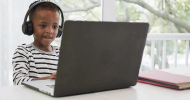 İnternette bilgisayar ve kulaklık kullanan mutlu Afrikalı Amerikalı çocuk, ağır çekimde. Eğitim, okul, çevrimiçi öğrenme, yaşam tarzı, çocukluk, iletişim ve ev hayatı, değiştirilmemiş.