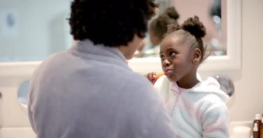 Afro-Amerikan anne ve kızının dişlerini fırçalaması ve banyoda öpüşmesi, yavaş çekim. Yaşam tarzı, kişisel bakım, hijyen ve ev hayatı, değişmemiş..
