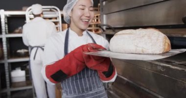 Fırın mutfağında çalışan çeşitli fırıncılar yavaş çekimde taze ekmek çıkarıyorlar. Takım çalışması, yemek, küçük işletme, fırın ve çalışma, değiştirilmemiş.