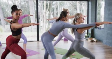 Çeşitli kadın eğitmenler yoga sınıfında Savaşçı 2 pozu için kadınlara yardım ediyor. Değiştirilmemiş, yavaş çekim, yoga, egzersiz, fitness, zen, sağlıklı yaşam tarzı ve refah kavramı.