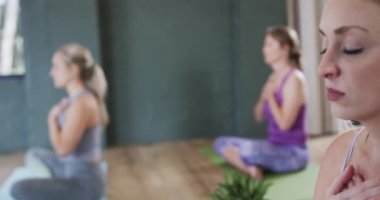 Elleri göğsünde olan çok ırklı kadınlar yoga stüdyosunda nefes egzersizi yapıyorlar. Değiştirilmemiş, yavaş çekim, yoga, egzersiz, fitness, zen, meditasyon ve refah kavramı.