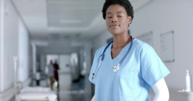 Afro-Amerikan kadın doktor hastane koridorunda gülümsüyor, ağır çekimde. Hastane, ilaç, sağlık ve iş, değiştirilmemiş.