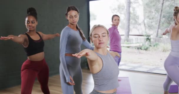 ヨガクラスで戦士2ポーズを練習する女性を助ける多様な女性インストラクター 変更されていない スローモーション フィットネス 健康的なライフスタイル 笑顔と幸福 — ストック動画