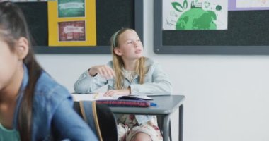 Masada oturan sıkılmış beyaz bir kızın sınıfın penceresinden fotokopi çekerken videosu. Eğitim, çocukluk, kapsayıcılık, ilkokul ve öğrenim kavramı.