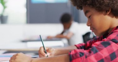 Çeşitli okul çocukları okul sınıfında yazı yazıyor ve masalarda oturuyorlardı. Eğitim, kapsayıcılık, ilkokul ve öğrenim kavramı.