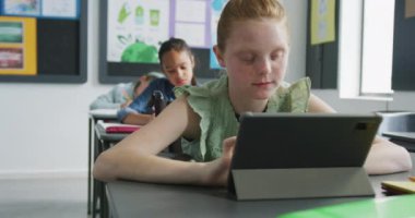 Masada oturan beyaz bir kızın okul sınıfında farklı tabletlerle fotokopi çekerken videosu. Eğitim, çocukluk, kapsayıcılık, ilkokul ve öğrenim kavramı.