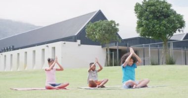 Farklı liseli kızların ve okul çocuklarının açık havada yoga meditasyonu yaptığı bir video, fotokopi odası. Eğitim, çocukluk, kapsayıcılık, sağlık, ilkokul ve öğrenim kavramı.