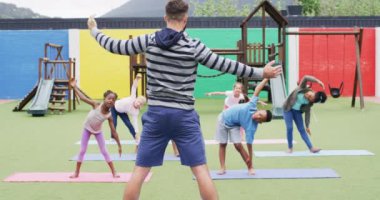 Çeşitli erkek öğretmenler ve okul bahçesinde paspaslar üzerinde egzersiz yapan mutlu öğrenciler. Eğitim, kapsayıcılık, ilkokul ve öğrenim kavramı.