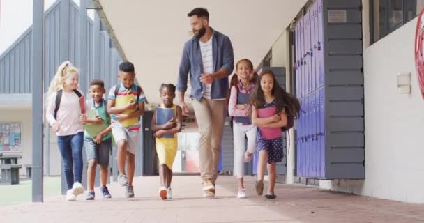 多様な男性教師と幸せな子供たちが学校を歩いています コミュニティ 小学校 学習コンセプト — ストック動画