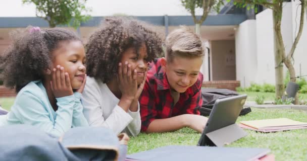 Video Van Drie Vrolijke Schoolkinderen Kijken Tablet Liggend Schoolplein Kopiëren — Stockvideo