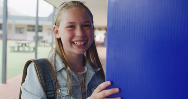 学校の廊下でロッカーを使用して幸せな白人女子高生のビデオ肖像画 コピースペース 幼少期 小学校 学習コンセプト — ストック動画