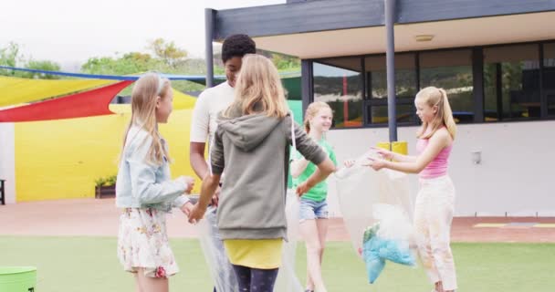 多様な女性教師と幸せな学校の子供たちが 学校の遊び場でバッグと一緒に掃除しています コミュニティ 小学校 学習コンセプト — ストック動画