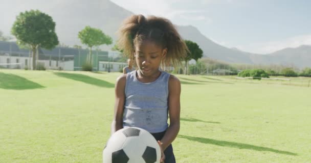 フィールドでフットボールを保持するアフリカ系アメリカ人の女子高生の笑顔のビデオ肖像画 幼少期 スポーツ 学習コンセプト — ストック動画