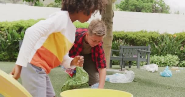校庭でリサイクルするためのゴミを集める2人の幸せな多様なスクールボーイのビデオ 幼少期 エコロジー 小学校 学習コンセプト — ストック動画