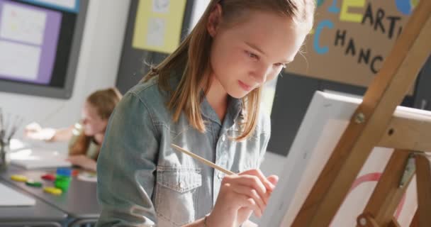 アートクラスのイーゼル絵画に立っている幸せな白人女子高生のビデオ コピースペース 幼少期 包摂性 創造性 小学校 学習コンセプト — ストック動画