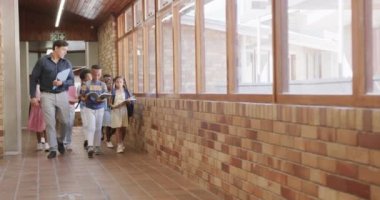 İlkokul koridorunda kitapları olan çeşitli erkek öğretmenler ve çocuklar, yavaş çekim. Okul, öğrenme, çocukluk, öğretim ve eğitim, değiştirilmemiş.