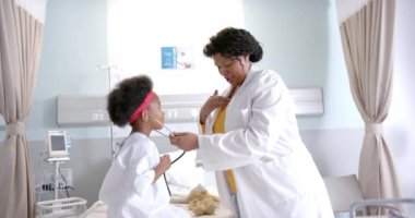 Mutlu Afro-Amerikan kadın doktor hastane odasında kızla oynaşıyor, ağır çekimde. İlaç, sağlık hizmetleri, çocukluk ve hastane, değiştirilmemiş.