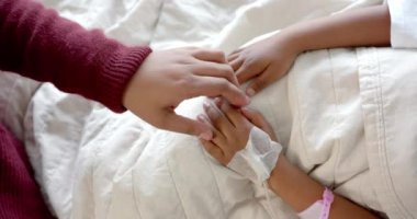 Holding hands of african american mother and daughter lying in hospital bed, slow motion. Medicine, healthcare services, family, childhood and hospital, unaltered.