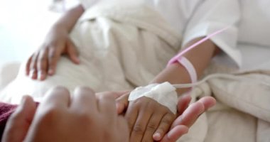 Holding hands of african american mother and daughter lying in hospital bed, slow motion. Medicine, healthcare services, family, childhood and hospital, unaltered.