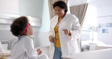 Afro-Amerikalı kadın doktor hastane odasında kızla beşlik çakıyor, ağır çekimde. İlaç, sağlık hizmetleri, çocukluk ve hastane, değiştirilmemiş.