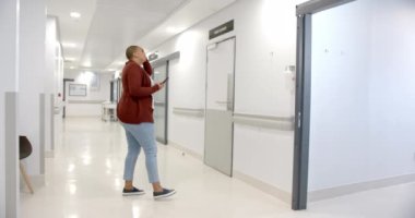 Stressed african american woman using smartphone in hospital corridor, slow motion. Medicine, healthcare services, communication and hospital, unaltered.