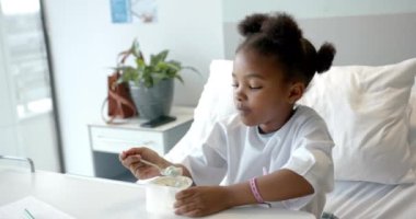 African american girl eating lunch in hospital bed, slow motion. Medicine, healthcare services, childhood, food and hospital, unaltered.