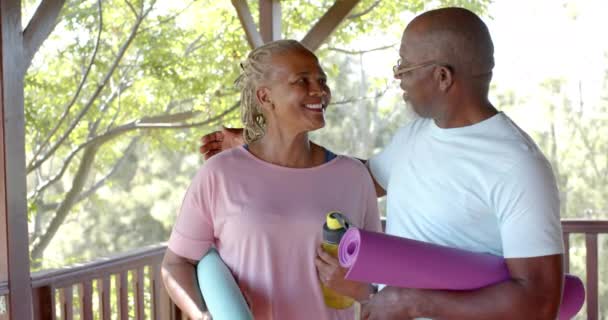 Happy Senior African American Couple Holding Mats Embracing Sunny Terrace — стоковое видео
