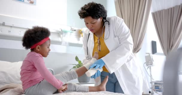 African American Female Doctor Putting Bandage Girl Leg Hospital Room — Stock Video