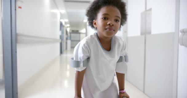 African American Girl Hospital Gown Walking Using Crutches Hospital Corridor — стоковое видео