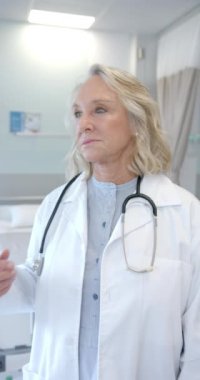 Vertical video of portrait of caucasian senior female doctor smiling at hospital. Medical healthcare concept