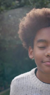 Vertical video of portrait of happy biracial boy smiling in garden, slow motion. Childhood, autumn and leisure, unaltered.