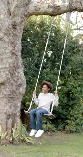Vertical Video Happy Biracial Boy Swinging Tree Swing Garden Slow — стоковое видео