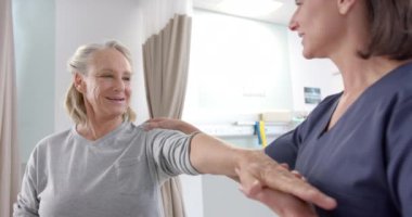 Caucasian female physiotherapist stretching hand of female senior patient at rehab center. Physiotherapy rehabilitation and medical healthcare concept