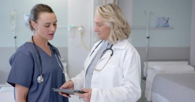 Caucasian female doctors in discussion using tablet in hospital room, slow motion. Medicine, healthcare services, communication and hospital, unaltered.