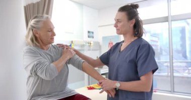 Caucasian female physiotherapist stretching hand of female senior patient at rehab center. Physiotherapy rehabilitation and medical healthcare concept