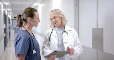 Caucasian female doctors in discussion using tablet in hospital corridor, slow motion. Medicine, healthcare services, communication and hospital, unaltered.